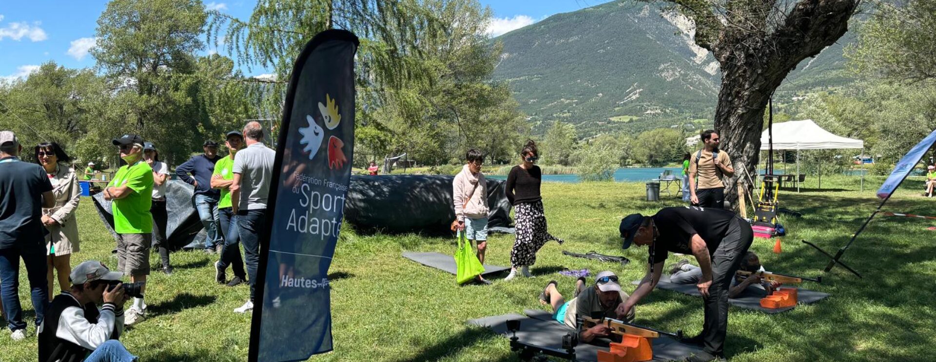 Activité découverte du tir à la carabine organisée par le comité de sport adapté. Des sportifs sont allongés dans l'herbe, par une belle journée d'été, dans les Hautes-Alpes, avec une montagne en fond.