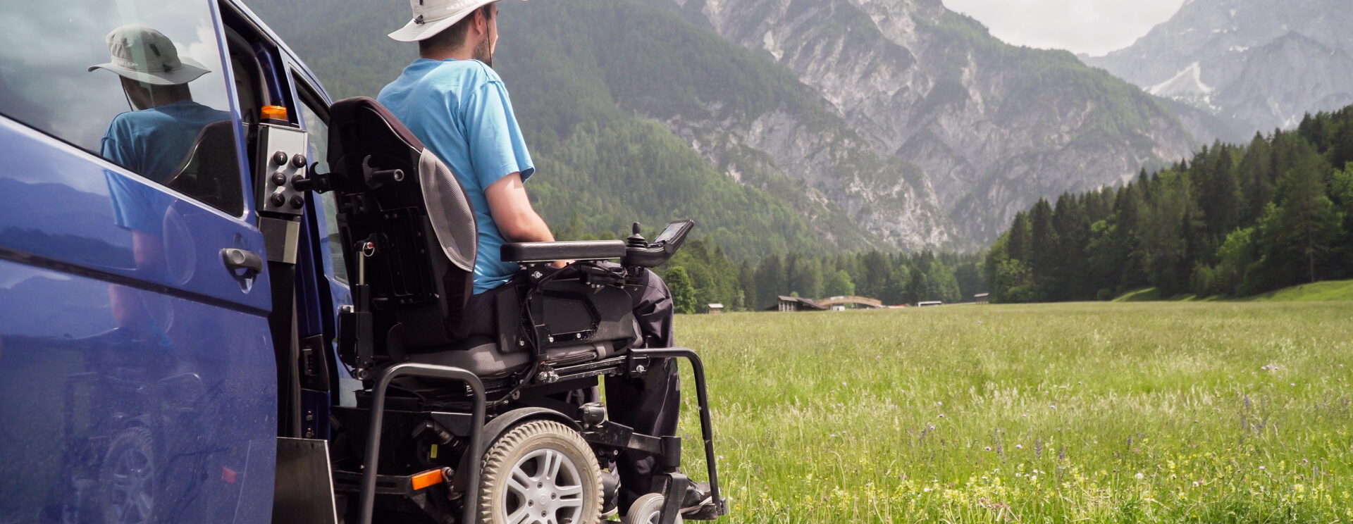 Homme en fauteuil descendant d'un véhicule aménagé, et contemplant la montagne