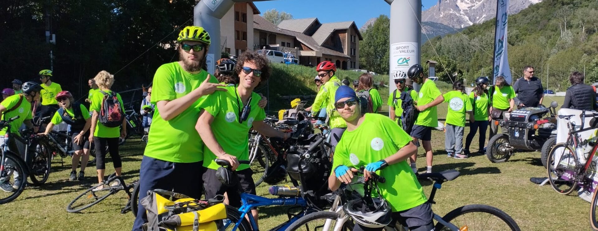 Photos de sportifs pendant la Traversée des Hautes-Alpes, en 2024, organisée par le Comité départemental de sport adapté. Les sportifs sont souriants, en t-shirt vert fluo, avec un vélo, devant l'arche d'arrivée, sous un beau ciel bleu.
