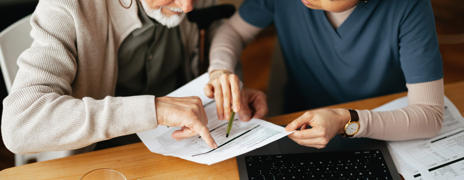 Jeune femme aidant un homme âgé à comprendre un document, écrit, devant un ordinateur