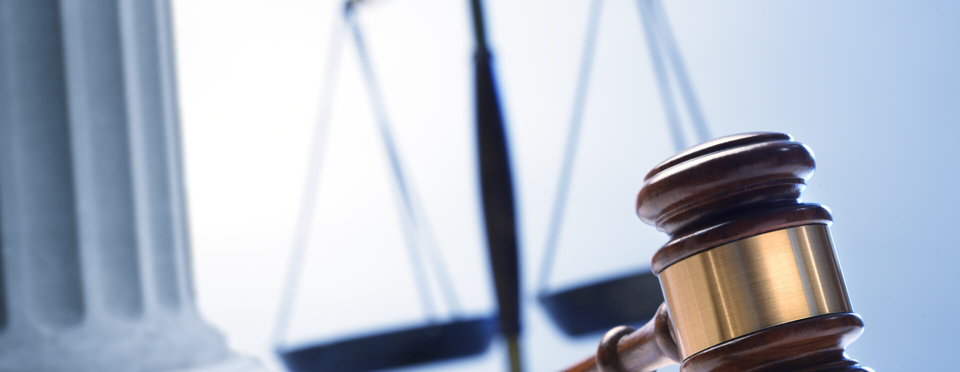 Au premier plan, un marteau du juge et un livre ouvert, au second plan, on distingue la balance de la justice